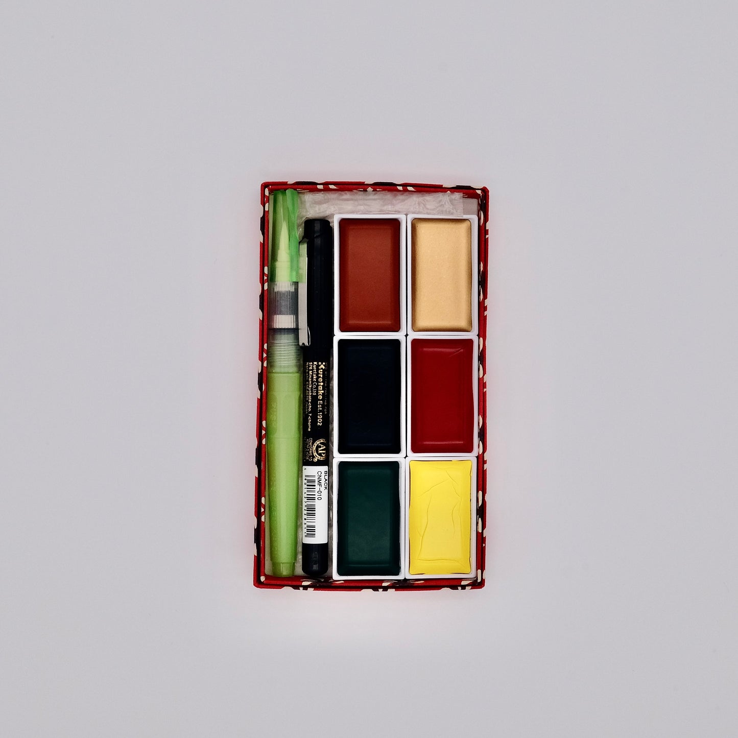 Set of watercolor paints with a brush in a rectangular box on a light gray background