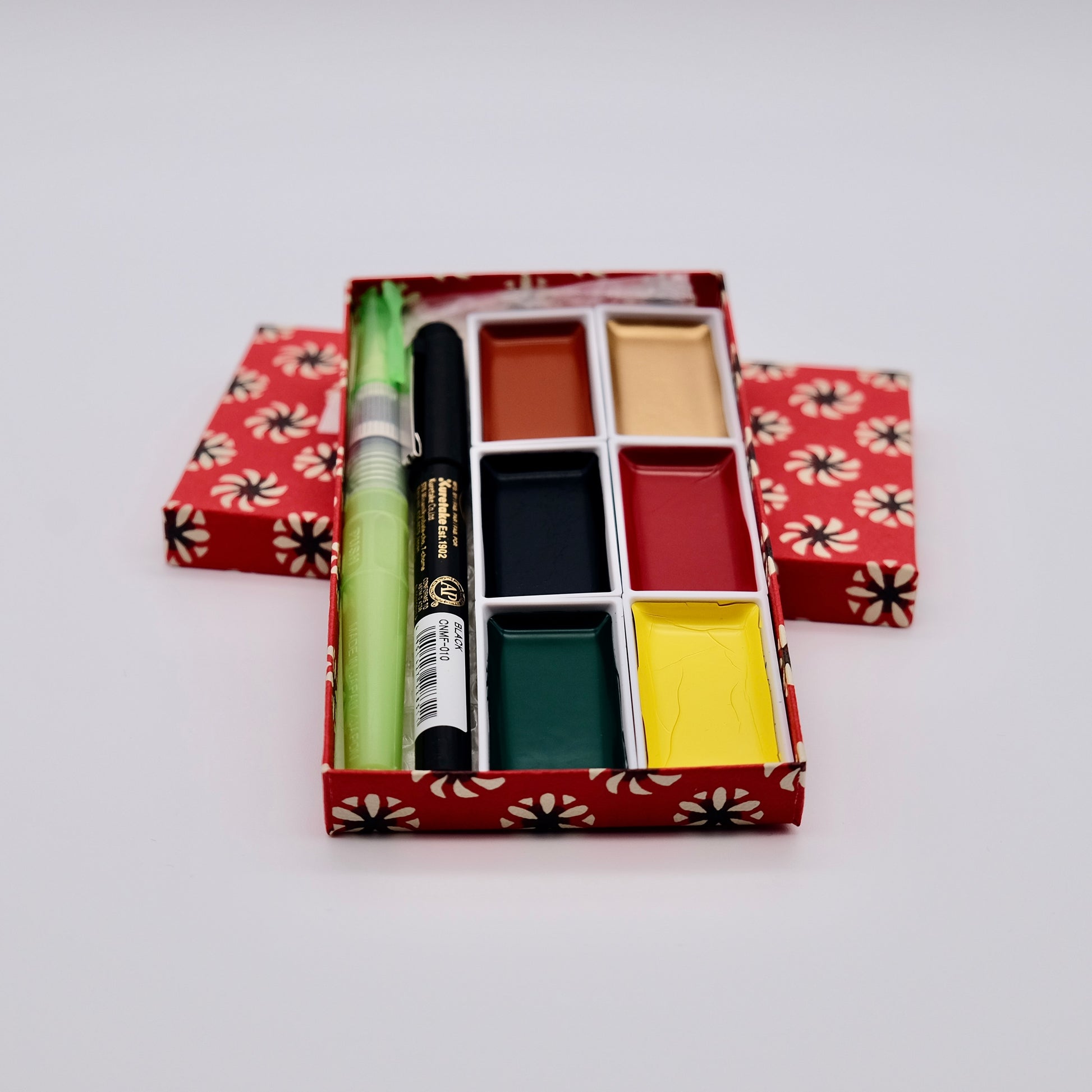 Set of watercolor paints and brushes in a decorative box on a white background