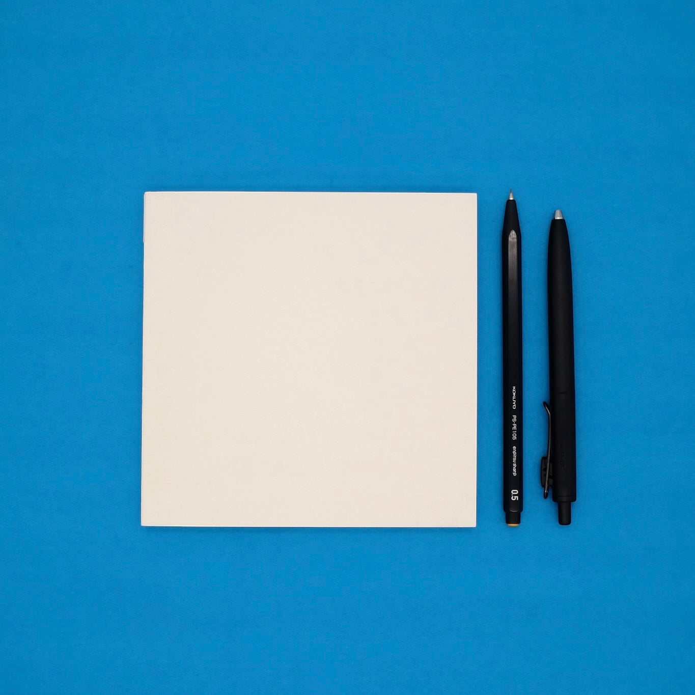 White notebook and two black pens on a blue background