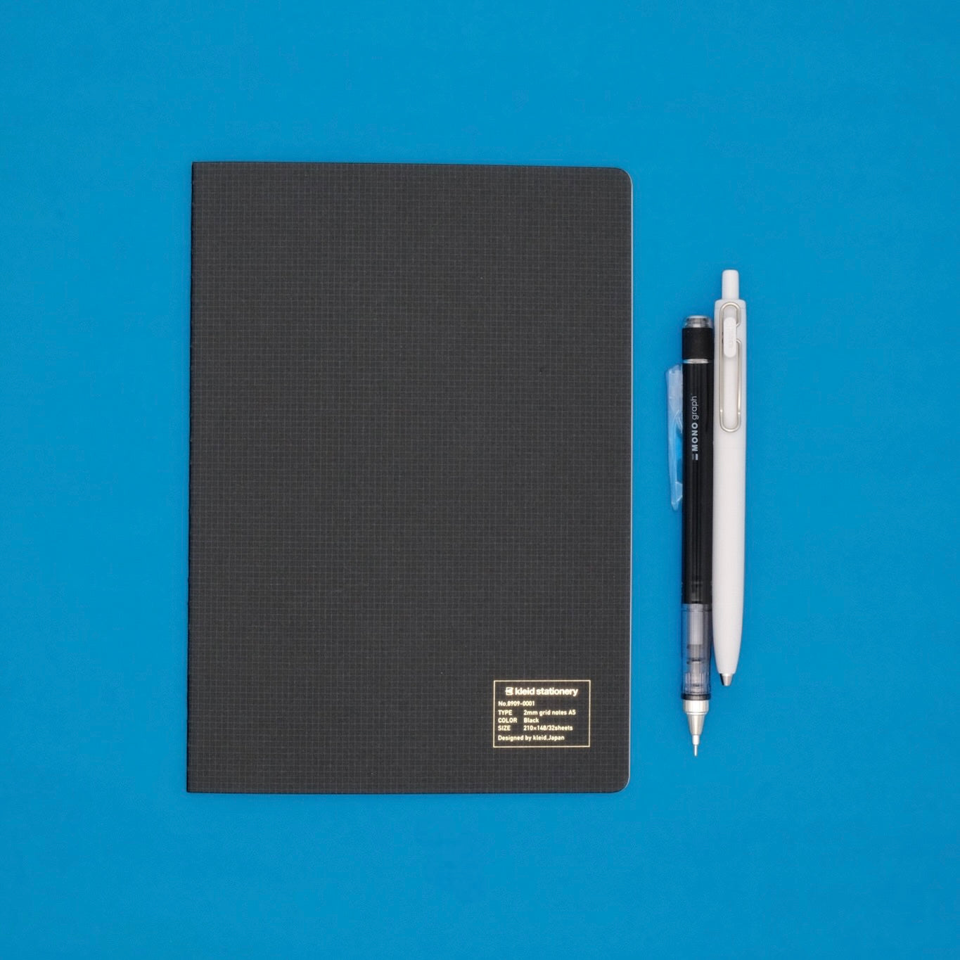 Black notebook with two pens on a blue background