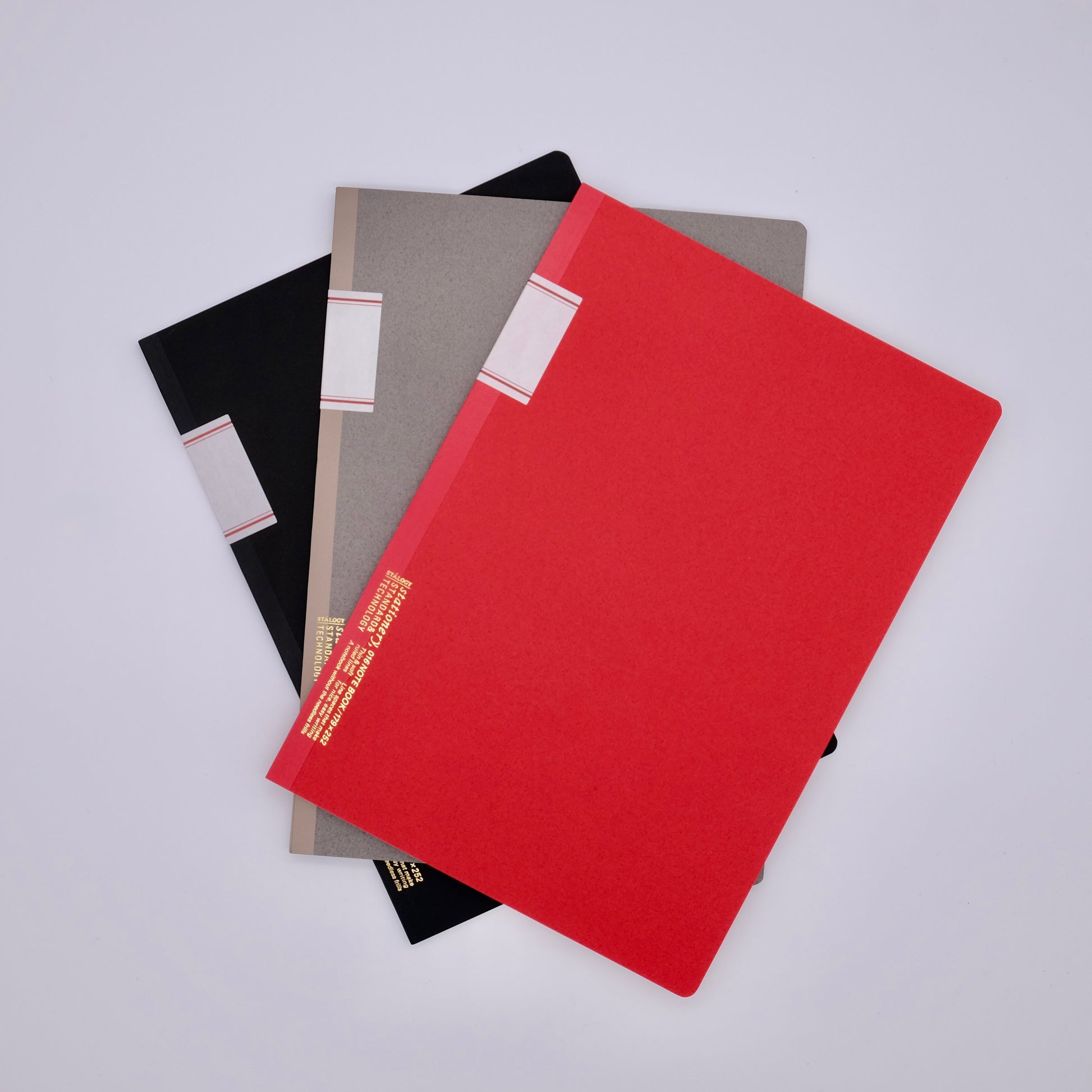 Three notebooks in black, gray, and red on a light gray background